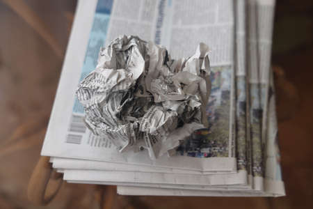 A crumpled sheet of newspaper lies on a stack of fresh newspapers, fake news, corrupt journalismの写真素材