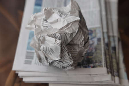 A crumpled sheet of newspaper lies on a stack of fresh newspapers, fake news, corrupt journalismの写真素材