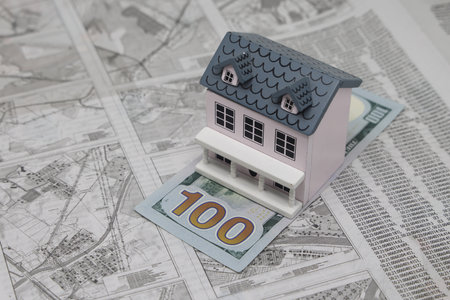A wooden model house stands on a dollar bill against the background of a land plot scheme, real estate purchaseの写真素材