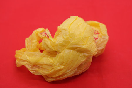 Crumpled yellow plastic bag from a supermarket on a red background, ecology, pollution