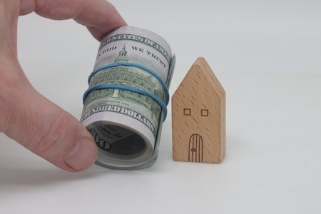 Rolled Dollar Banknotes For Buying House. House model and dollar banknote with alarm clock on white backgroundの写真素材