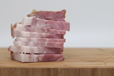 Slices of smoked bacon on a wooden cutting board on a white background. Pork shoulder meatの写真素材