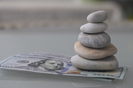 Pyramid of stones and euro banknotes. Stack of zen stones with hundred dollar bill on gray background. Rest on the seaの写真素材