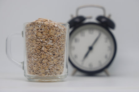 A glass with oatmeal against a background of a clock, morning porridgeの写真素材