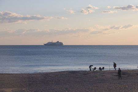 Fishermen on a sandy shore against the backdrop of the sea at sunset and a passenger ship on the horizon, Alanya, Turkey, March 2025の写真素材