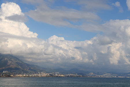 The coastline is built up with houses of a large city against the backdrop of the sea, mountains and white cloudsの写真素材