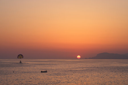 Sunset on the sea coast against the backdrop of mountains, calm sea and paraglider, peaceの写真素材