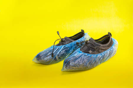 black sneakers in shoe covers on a yellow background.の写真素材