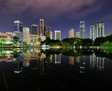 City park with modern buildings in Kuala Lumpur at night reflection in waterの写真素材