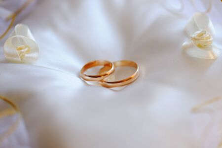 Pair of gold wedding rings on a white pillow.の写真素材