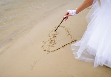 Bride drawing heart on the sand.の写真素材