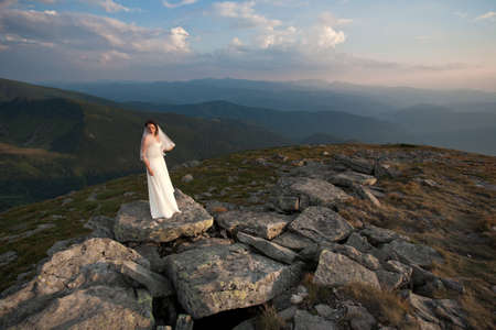 Bride in wedding dress standing high in mountains.の写真素材