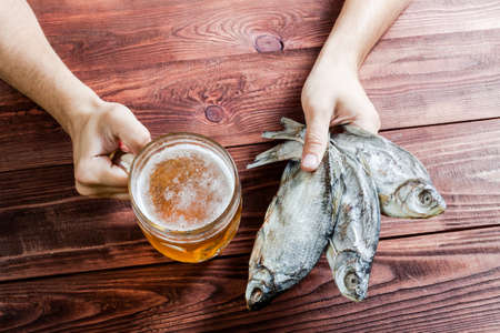 Male hand with a glass of beer and dried fish, traditional russian snack. Wooden background.