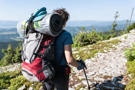 Hiker girl with backpack relaxing on top of a mountain and enjoying valley view.