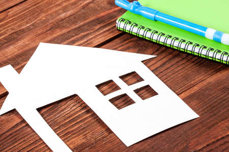 White paper house figure with notebook on wooden background.の写真素材