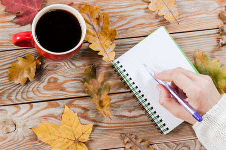 Coffee cup, notebook and autumn leaves on wooden background. Autumn and business background.