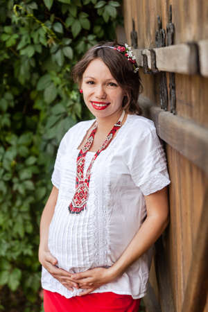 Ukrainian pregnant woman wear traditional embroidered shirt. Location in traditional ukrainian village. Pregnancy concept.の写真素材