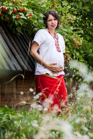 Ukrainian pregnant woman wear traditional embroidered shirt. Location in traditional ukrainian village. Pregnancy concept.の写真素材