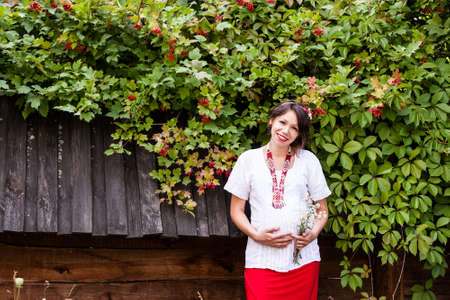 Ukrainian pregnant woman wear traditional embroidered shirt. Location in traditional ukrainian village. Pregnancy concept.の写真素材