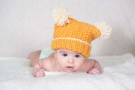 Beautiful newborn baby girl with funny yellow hat, lying in her bed and smiling.