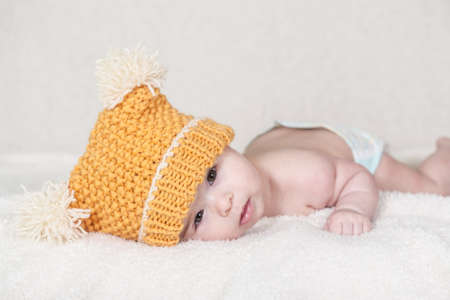 Beautiful newborn baby girl with funny yellow hat, lying in her bed and smiling.