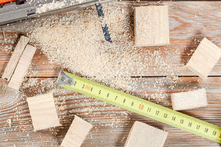 Electric jigsaw with many wooden bricks full of sawdust. On old scratched wooden table, work tools...