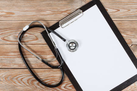 Medical clipboard and stethoscope on wooden table background. Top view. Health care and medicine...