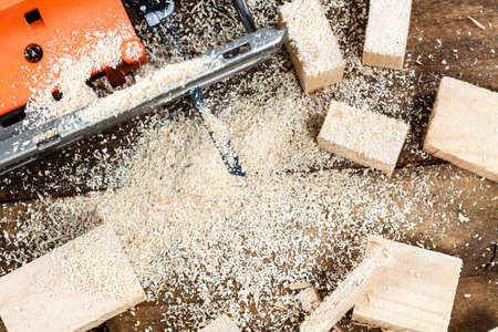 Electric jigsaw with many wooden bricks full of sawdust. On old scratched wooden table, work tools...