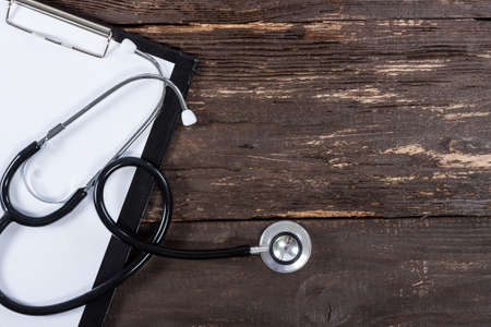 Medical clipboard and stethoscope on old dark wooden table background. Top view. Health care and medicine concept.の写真素材