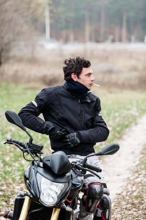 Biker sitting on motorcycle on an empty road, and smoking his cigarettes. Transportation concept.の写真素材