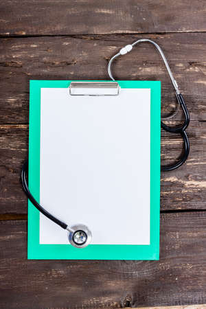 Medical clipboard and stethoscope on old dark wooden table background. Top view. Health care and medicine concept.の写真素材