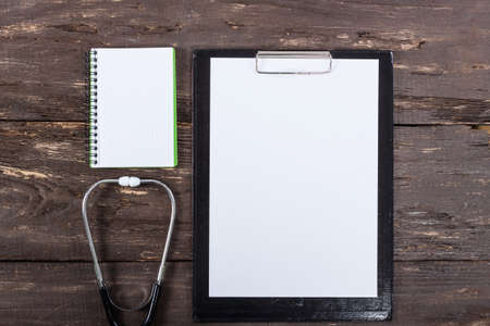 Medical clipboard and stethoscope on old dark wooden table background. Top view. Health care and medicine concept.の写真素材