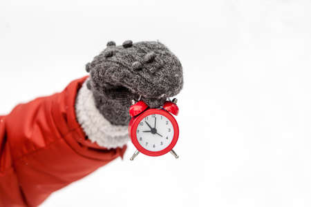 Hand holding red alarm clock over snow background.の写真素材