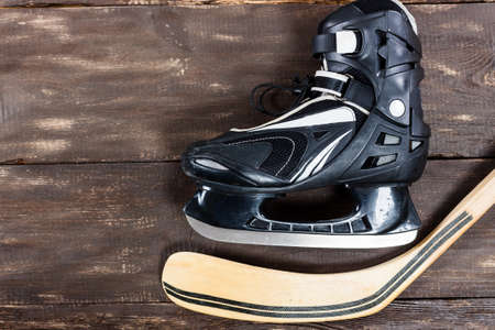 Overhead view of hockey stick and ice skates placed on old rustic wooden table. Winter sport leisure...