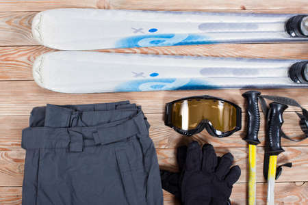 Overhead view of ski accessories placed on rustic wooden table. Items included ski, goggles, gloves and pants. Winter sport leisure time concept.の写真素材