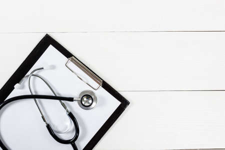 Medical clipboard and stethoscope on white wooden table background. Top view. Health care and medicine concept.の写真素材