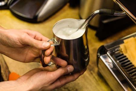 Barista preparing milk for takeaway coffee. Close-up view on hands, small coffee business concept.の写真素材