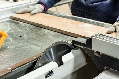 Worker using saw machine to make furniture at carpenters workshop. Handmade business at small...