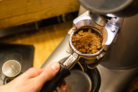 Barista grinds coffee beans in a coffee grinder. Close-up view on hands with portafilter, barista...