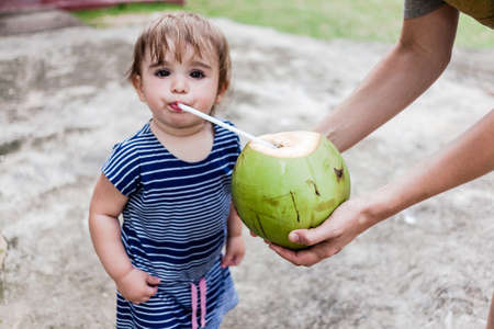 Cute little girl drinking coconut. Beach holidays conceptの写真素材