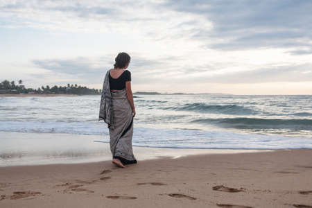 Beautiful young girl dressed in a sari posing on the beachの写真素材