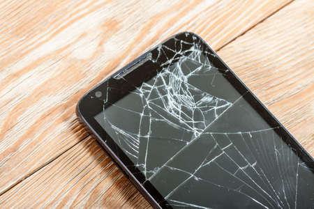 Mobile smartphone with broken screen on wooden background.