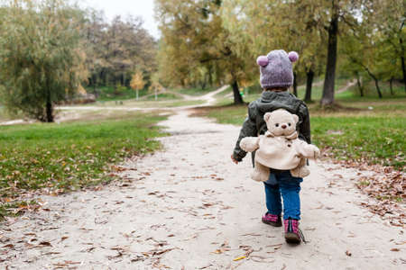 Little girl in autumn forest with teddy bear backpack. Fall day. Little girl exploring nature.の写真素材