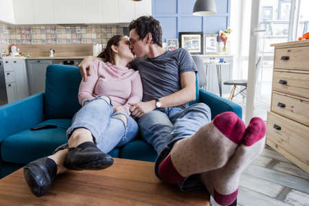 Romantic couple. Beautiful young loving couple embracing while sitting in big cozy sofa and watching...