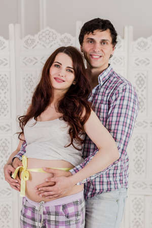 Pregnancy and people concept - happy man hugging his pregnant wife standing at home.の写真素材