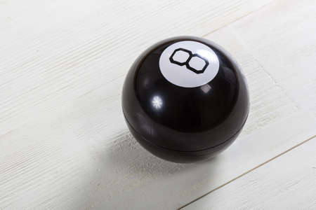 Magic prediction eight ball on white wooden background.