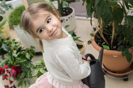 Cute little girl watering plants in her house. Child taking care of plants. Kid with water can.