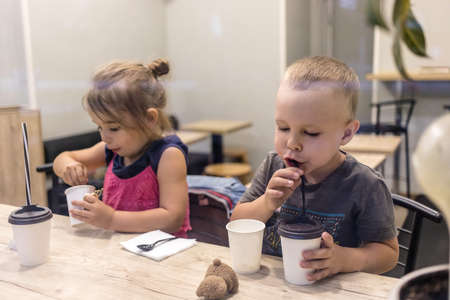 Two kids boy and girl, relaxing at the city cafeteria at evening. Drinking their child coffee, shot from the window.の写真素材