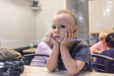 Little boy waiting for his order in cafe. Shot from the window.