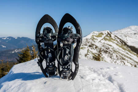 Winter hiking in the mountains. Black snowshoes in fresh show with snowflakes, at mountain view.の写真素材